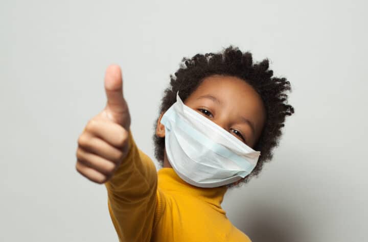 Child wearing a face covering giving a thumbs up